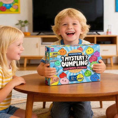 Two children at a living room coffee table, the older one holding the Mystery Dumpling Countdown Calendar box upright and laughing